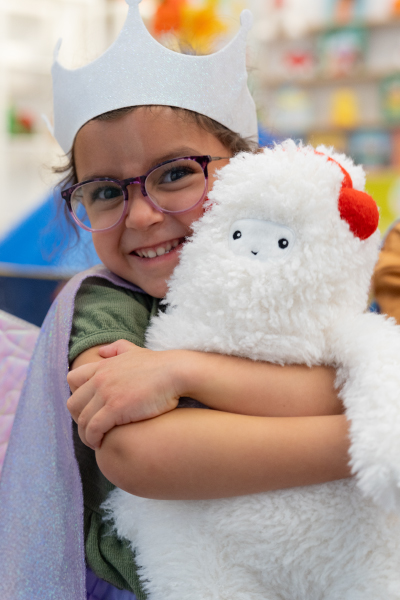 a little girl wearing a toy crown hugging a Gigglescape plush Yeti