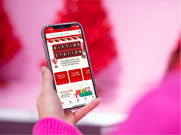 A woman in a pink sweater holds an iPhone displaying Target’s Gifting Station in the Target app.