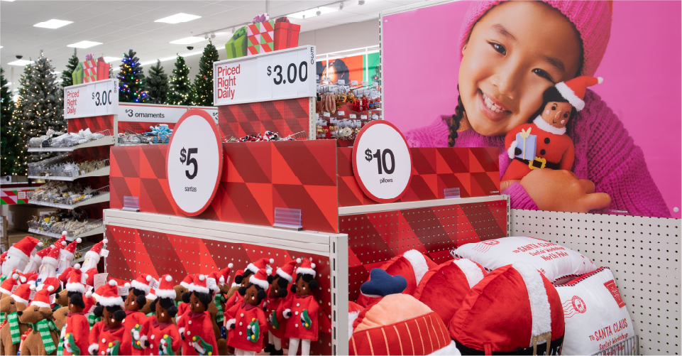 Colorful holiday shelves at Target with signs indicating $5 and $10 items, with a photo of a smiling young girl in the background.