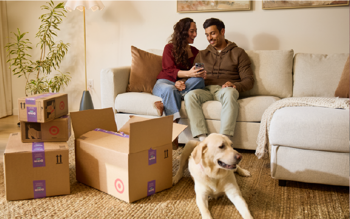 Two people sit on a couch next to a dog and several Target delivery boxes.