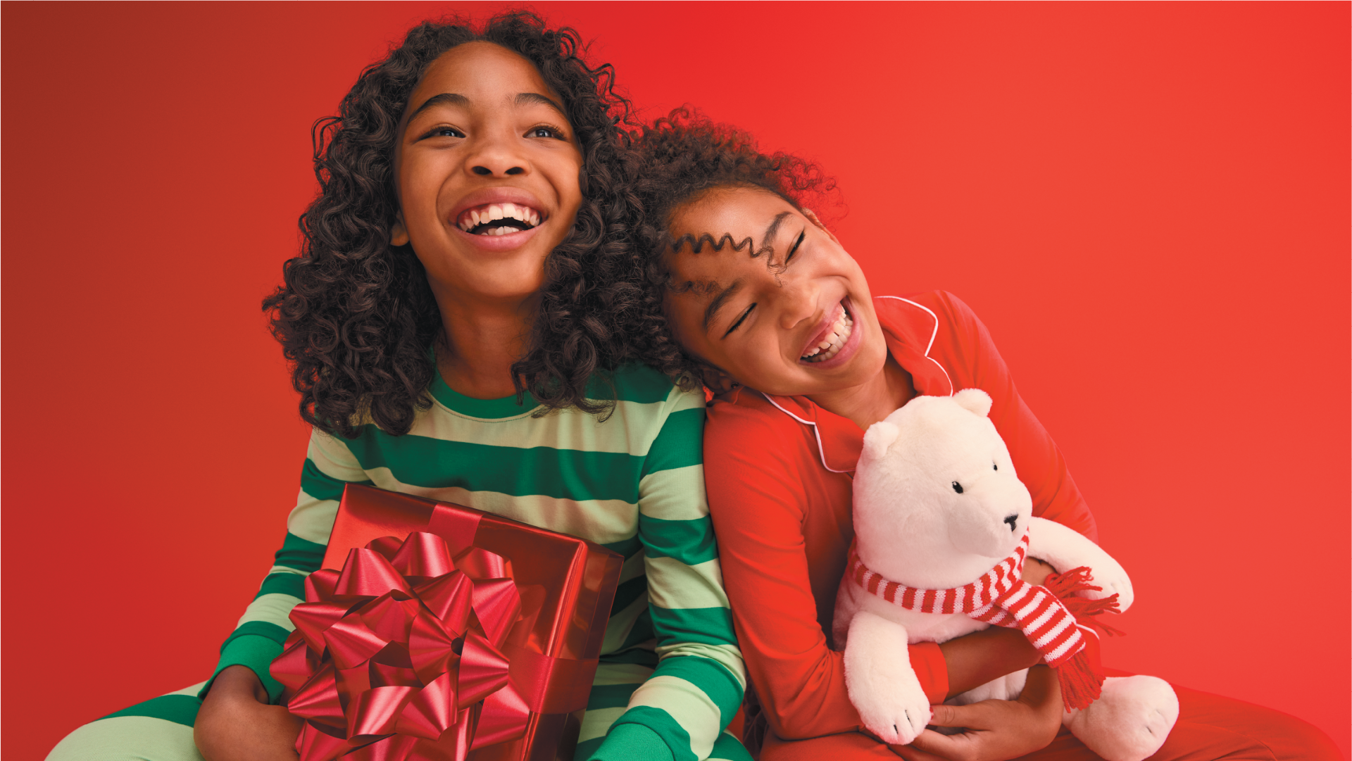 Two children smile wearing pajamas and holding holiday toys.