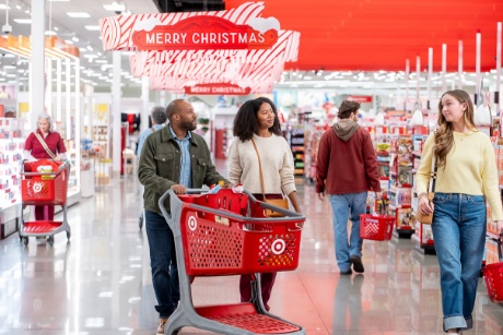 Target guests are walking with a Target cart beneath festive “Merry Christmas” signage.