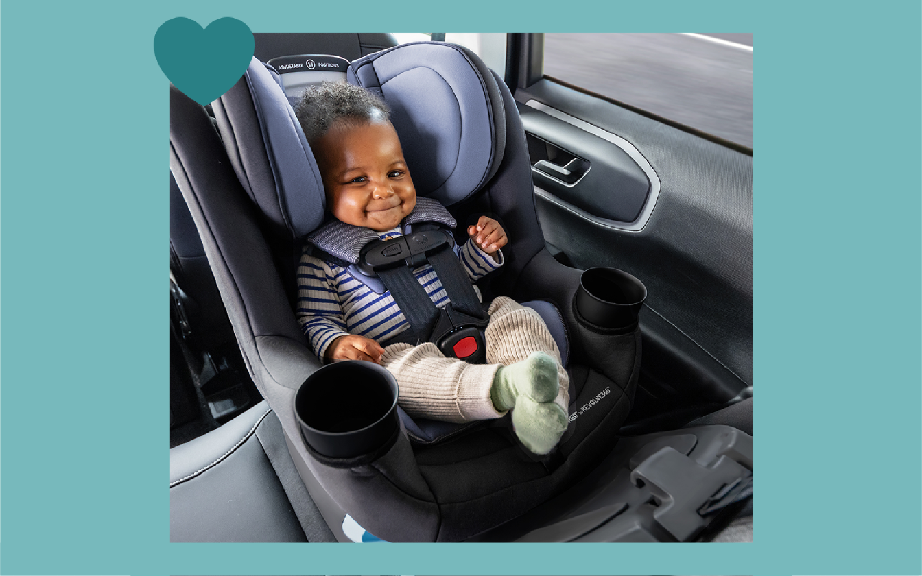 A baby sits smiling in a car seat.