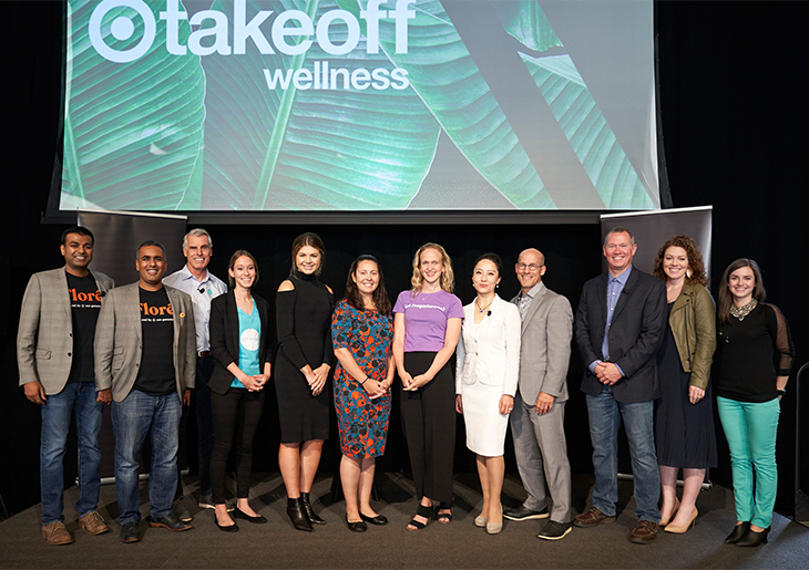 Twelve men and women representing the startups taking part in the accelerator stand onstage together in front of a screen that reads 'Target takeoff wellness