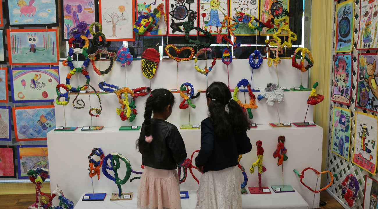 Two little girls examine a colorful display of children's art projects