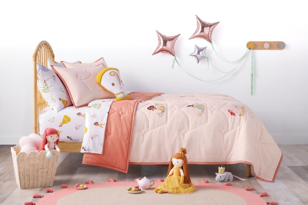 A kid’s bed displays a pink Disney Princess-themed comforter and Beauty and the Beast plush dolls.