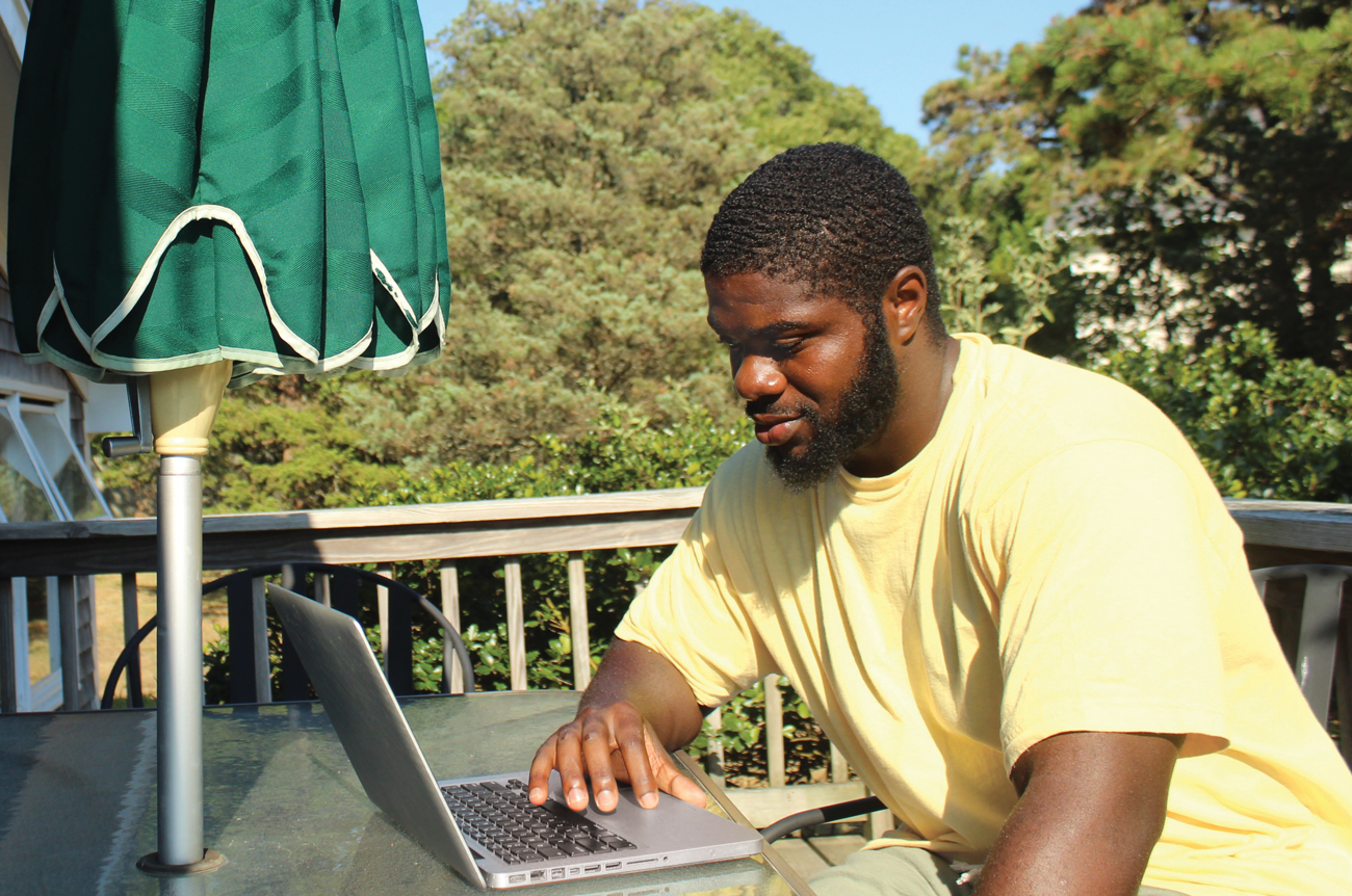Isaiah sits on a deck oustide with his laptop.