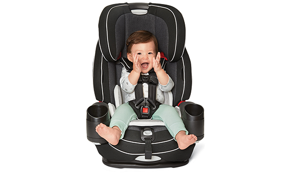 A baby smiles and claps sitting in a gray and black car seat