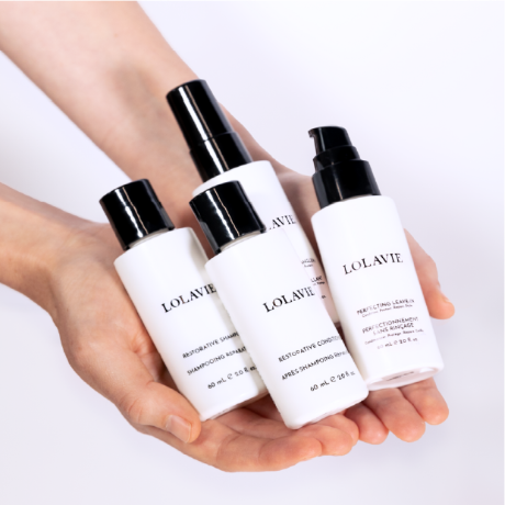 Two hands holding four bottles of LolaVie products.