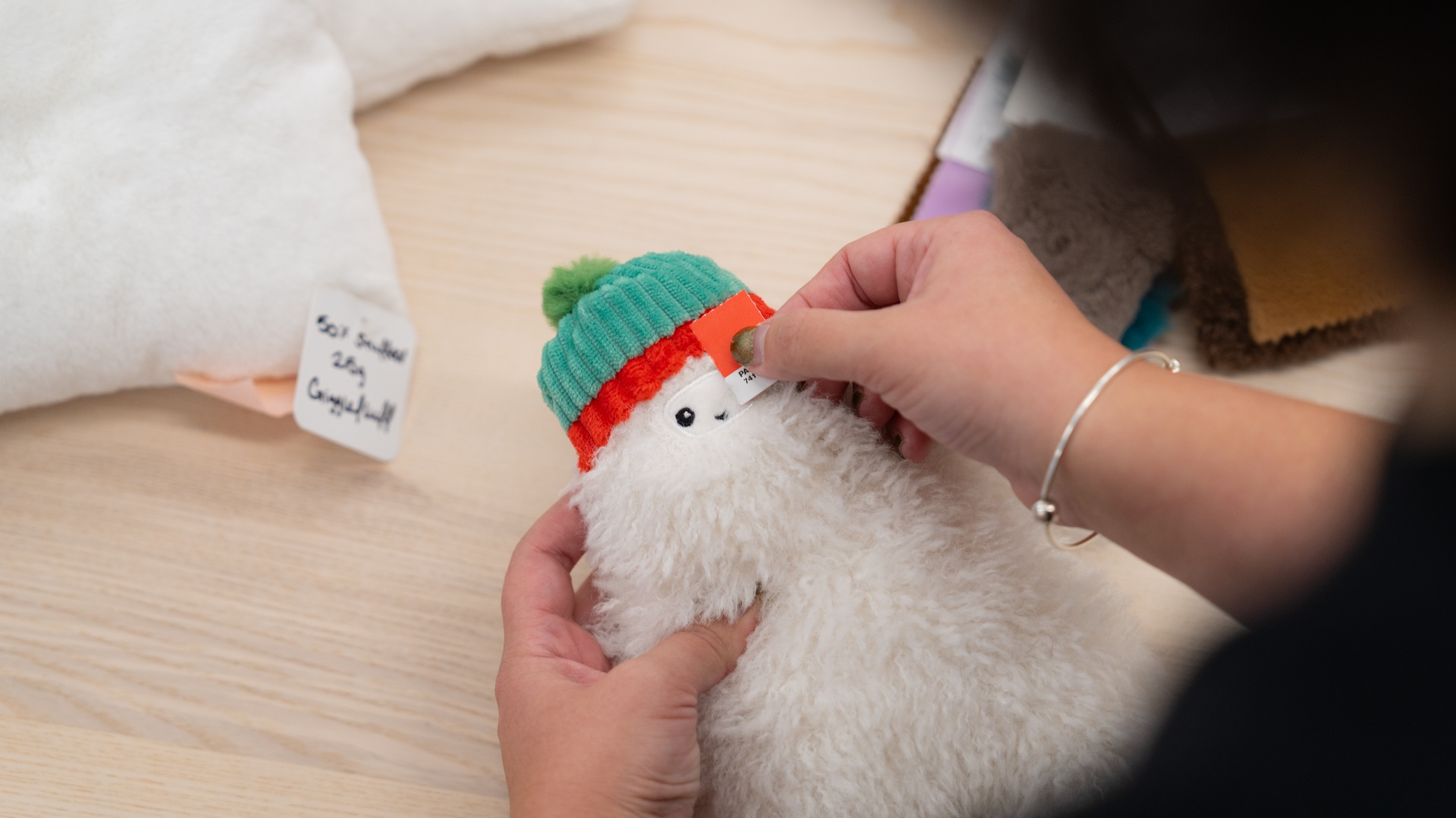 A person holds a Pantone color chip next to a Gigglescape yeti plush animal.