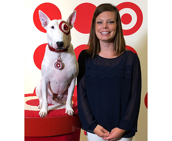 Emily F. sits next to Bullseye the dog in front of a red and white branded background
