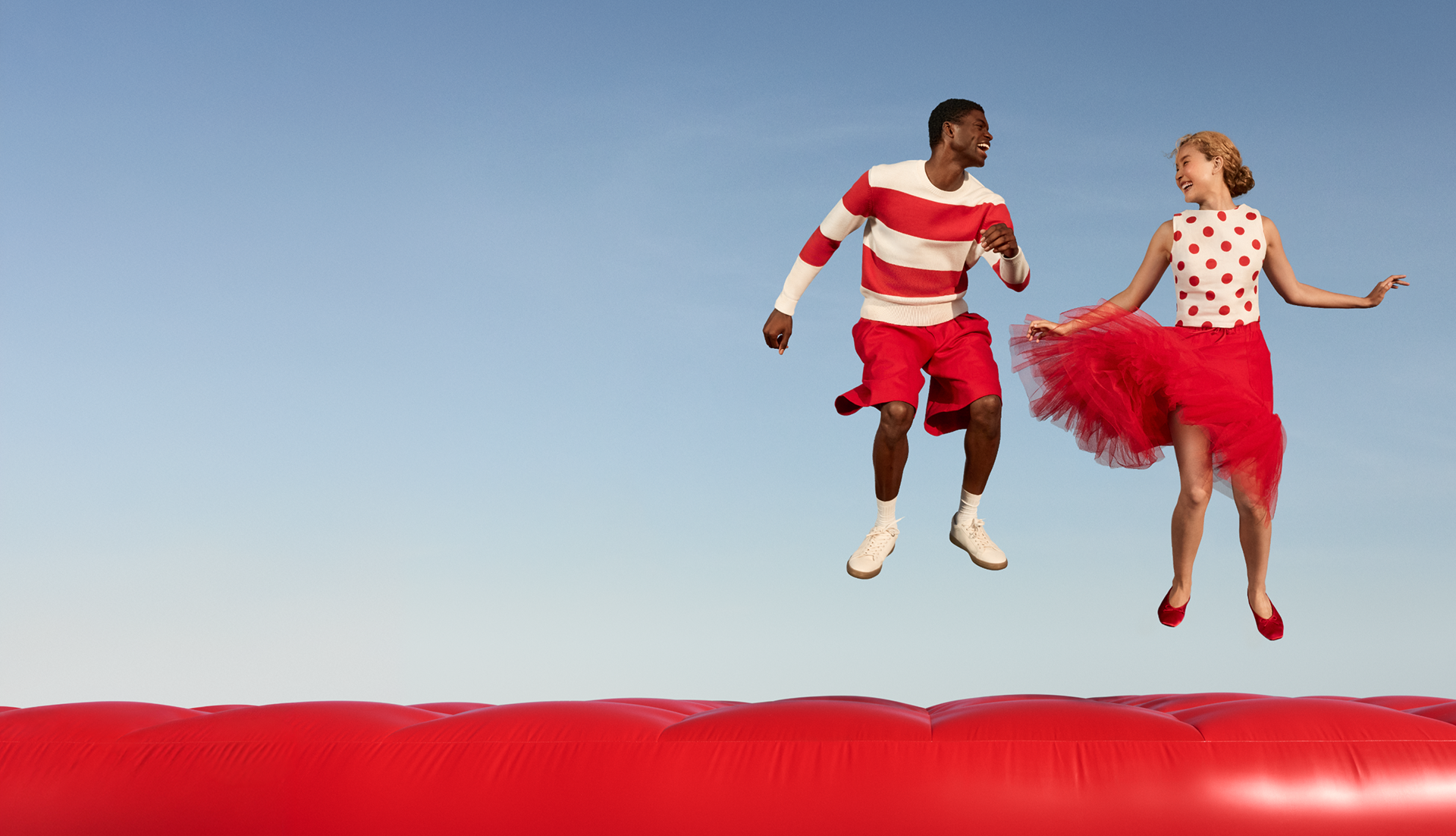 Two people wearing red and white jump on a large red inflatable object.
