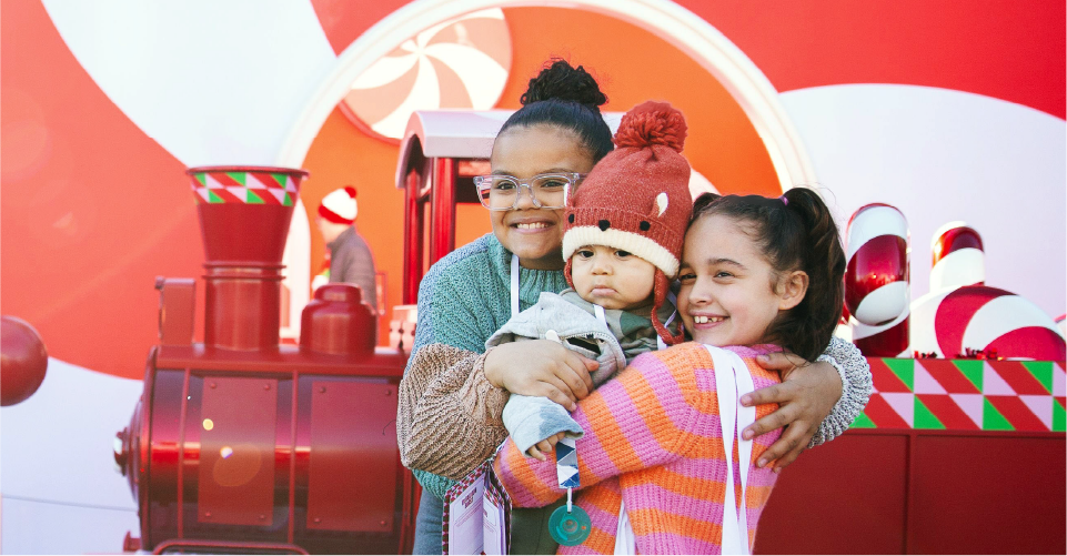 Three young Target guests stand in front of a holiday train engine at a Target Wonderland pop-up event.