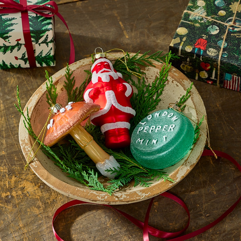 a wooden table with a wooden bowl containing three ornaments next two wrapped gifts