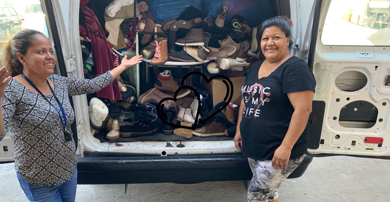 Two women smile in front a van filled with shoes and clothes