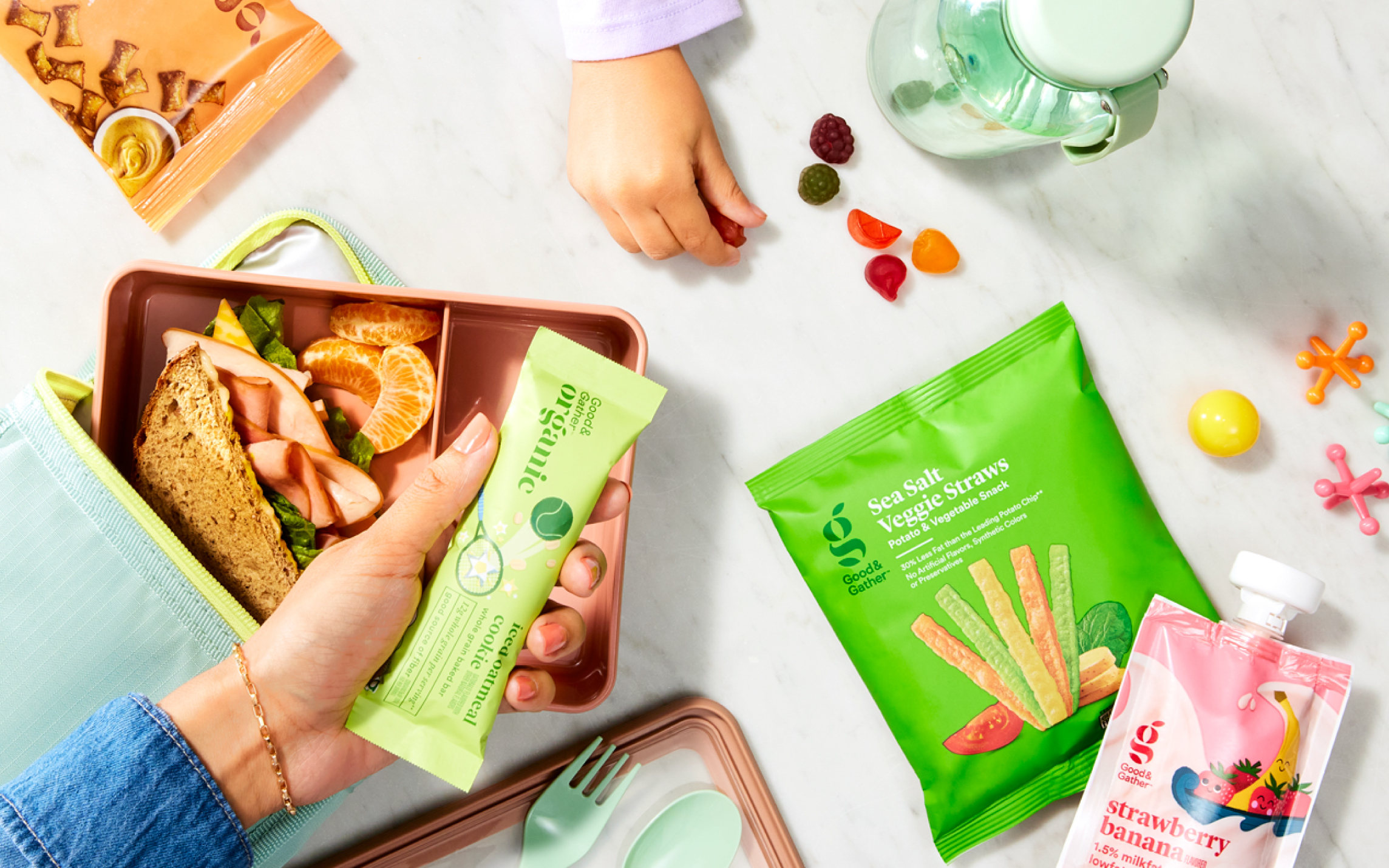 A lunchbox with a sandwich, fruit, and Good & Gather snacks, including applesauce, veggie straws, fruit snacks, and a handwritten lunch note.