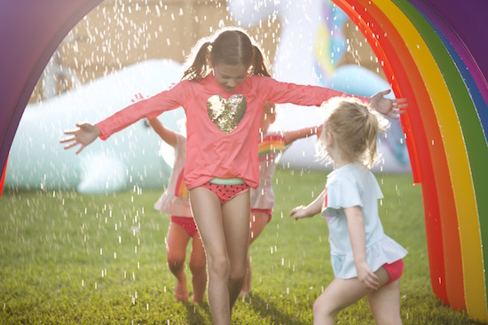 The girls run through a rainbow sprinkler