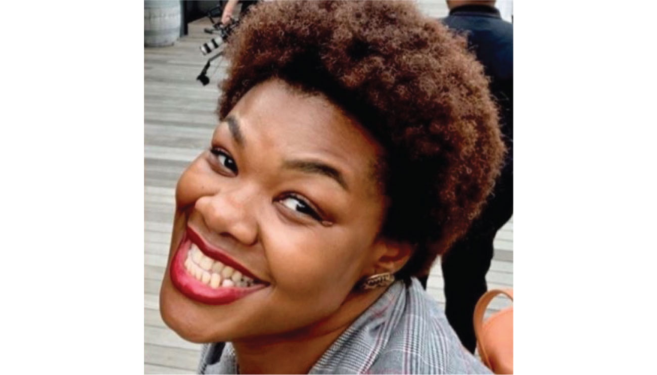 Flora smiles at the camera, wearing a striped jacket, gold earrings and bright red lipstick