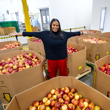 Kiera Fernandez poses among large boxes of apples.