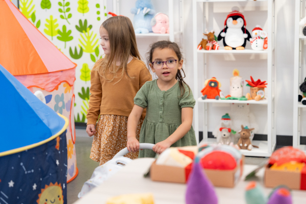 two little girls standing with Gigglescape toys and one is pushing a baby stroller