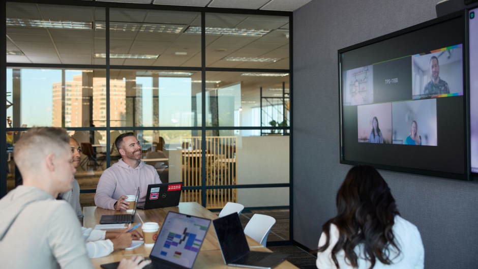 Multiple Target team members having a meeting at a desk with a screen showing virtual participants joining on Zoom.