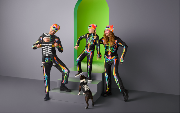 Two adults, a child, a baby and a dog wearing matching family skeleton costumes.