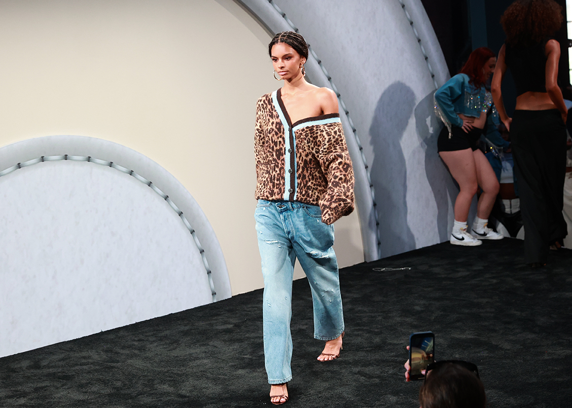 A model walks on a runway wearing jeans and an animal print sweater 