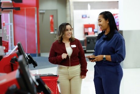 A team member at self-checkout smiles and stands next to a guest.