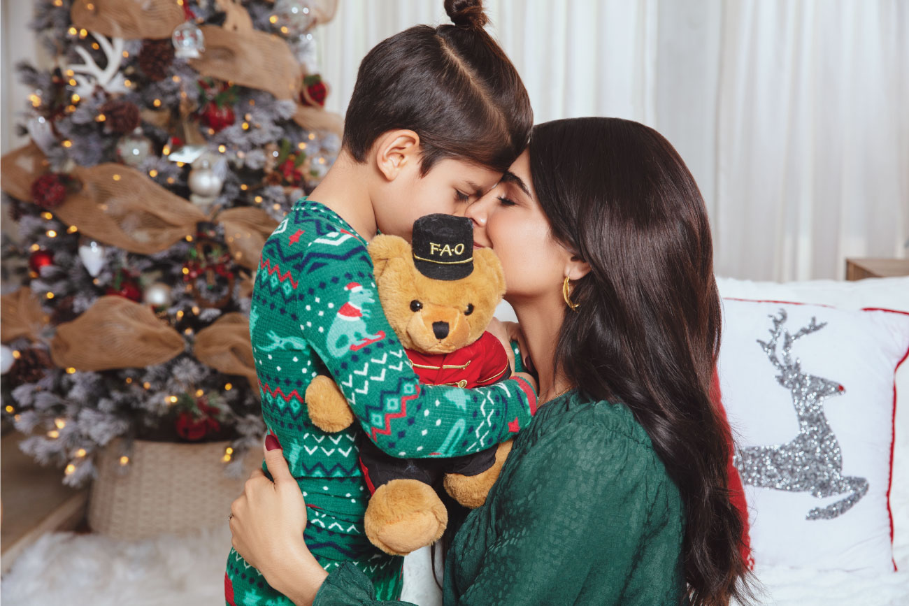 Alejandra hugs her son as he snuggles a teddy bear dressed as a toy soldier