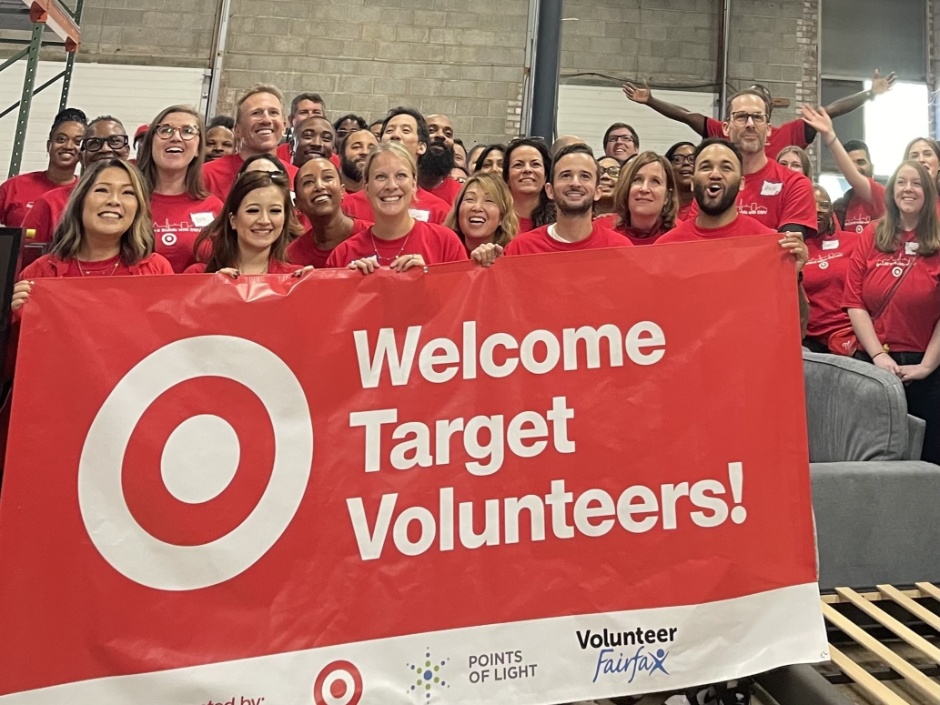 A group of Target team members in red shirts stand in a warehouse behind a banner that says “welcome Target volunteers!”