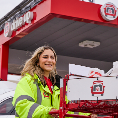 A Target team member wearing a yellow jacket smiles while pushing a cart at Drive Up.