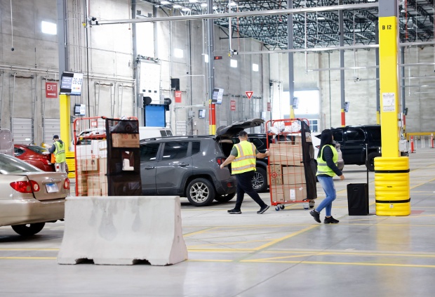 Three drivers wearing yellow vests bring guest orders to their vehicles.