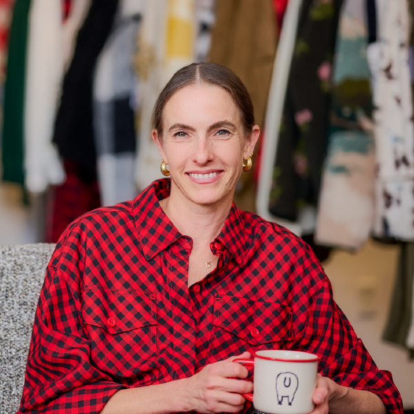 A background of Woolrich fabric swatches with a model looking through binoculars, wearing Woolrich x Target buffalo check jacket and skirt, with a t-shirt that has an image of a sheep