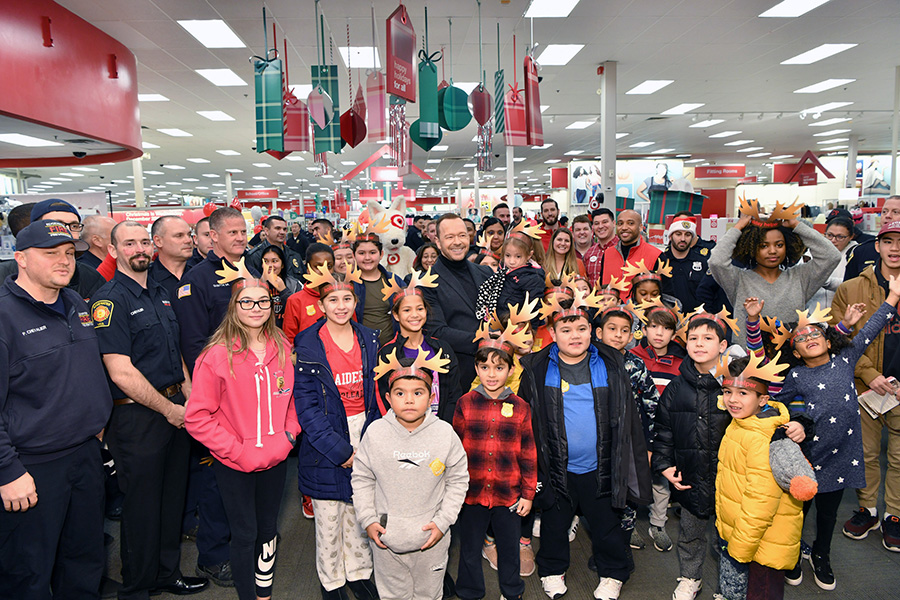 Donnie Wahlberg poses with a large group of officers, kids and team members. Many are in uniform and wearing paper reindeer antlers.