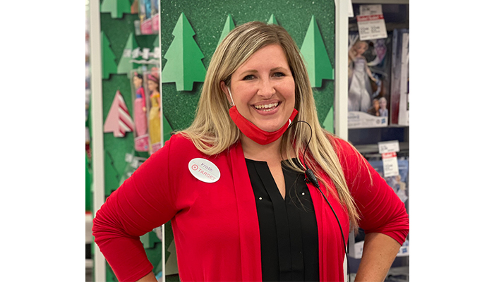 Kristin stands in front of a holiday display smiling and wearing a red shirt and mask pulled down at her chin.