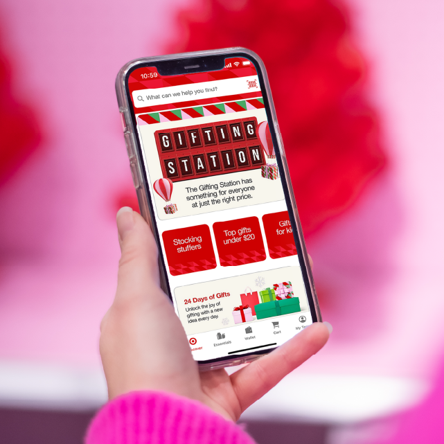 A woman in a pink sweater holds an iPhone displaying Target’s Gifting Station in the Target app.