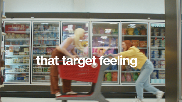 A person laughing while pushing another person in a Target cart, overlaid with the words "That Target feeling."