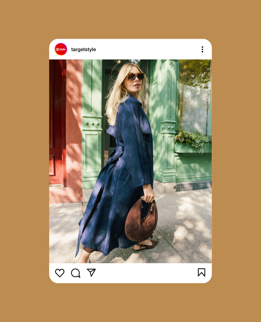 A screenshot of an Instagram post in which a model walks on a sidewalk wearing a long blue coat and carrying a brown suede bag.