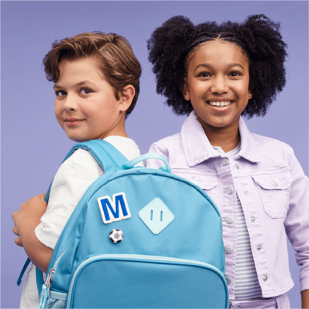 Two children smile wearing items from Target, including a backpack.