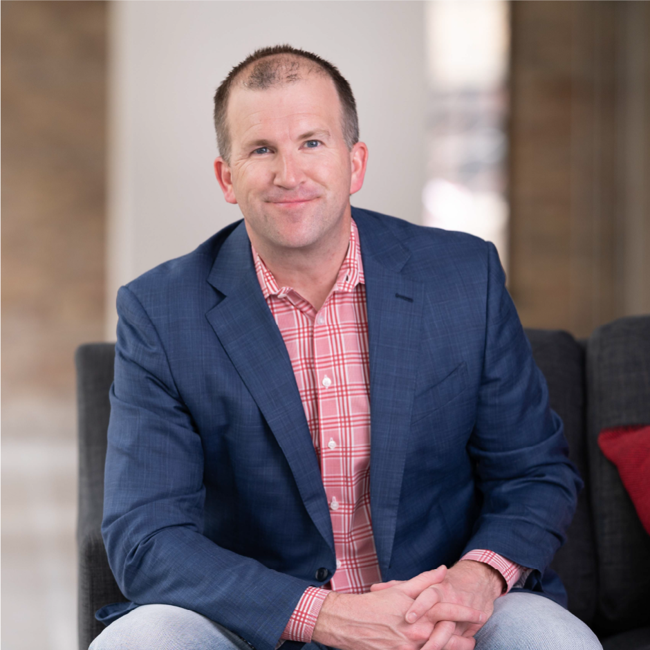 Michael Fiddelke sits on a couch leaning forward, smiling at the camera.