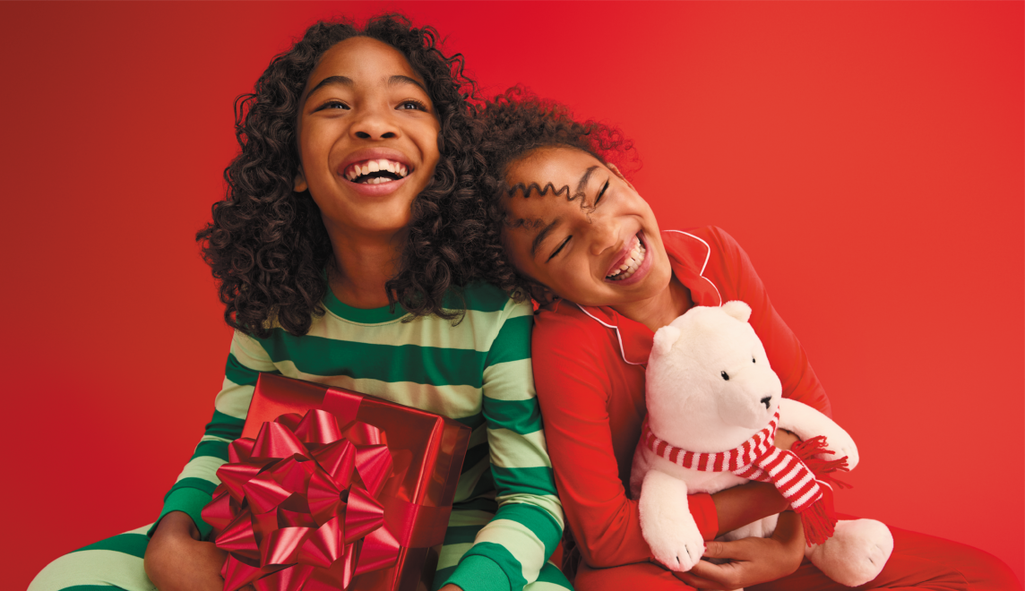 Two children smile wearing pajamas and holding holiday toys.