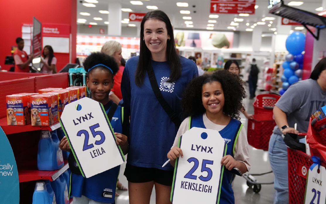 A woman smiles next to two children holding Minnesota Lynx signs.