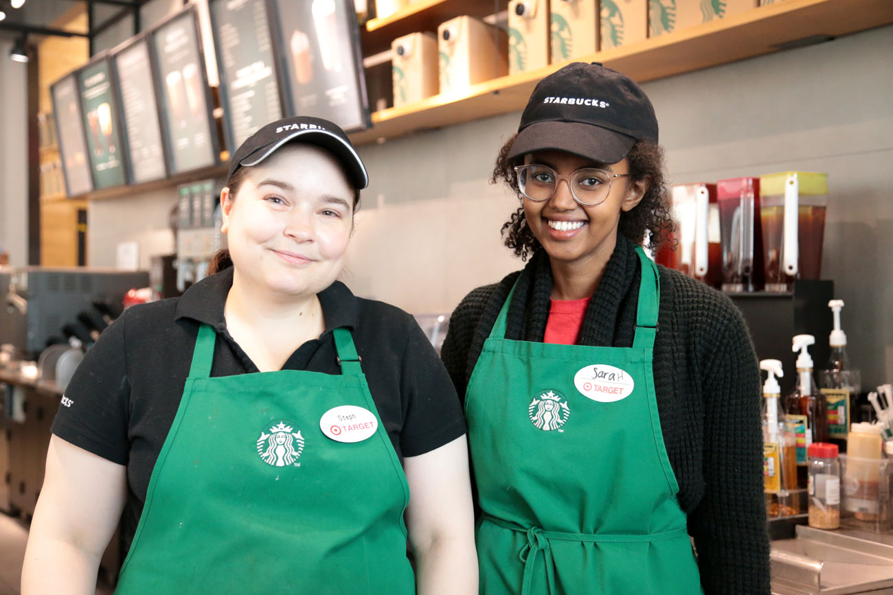 Two Starbucks employees wear green aprons and smile