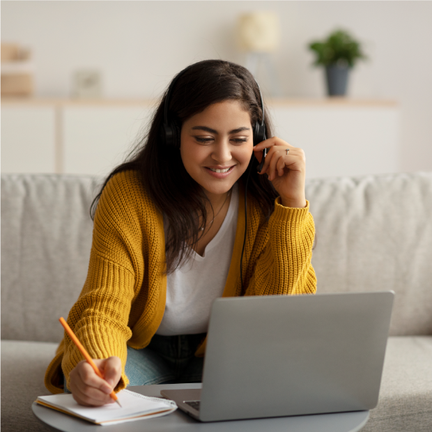 A person in a yellow sweater sits while working at a laptop.