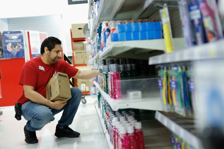 A team member crouches and stocks a shelf with mouthwash.