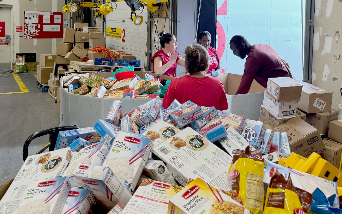 Four adults move and organize pallets of donated food.