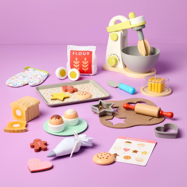 A white background displays a pan with cookies, a mixer, a dough roller, a cookie cutter and other toy baking essentials.