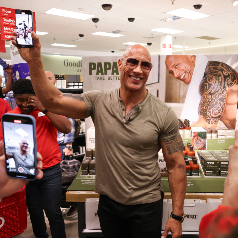 Dwayne "The Rock" Johnson smiles while holding a cell phone in a Target store.