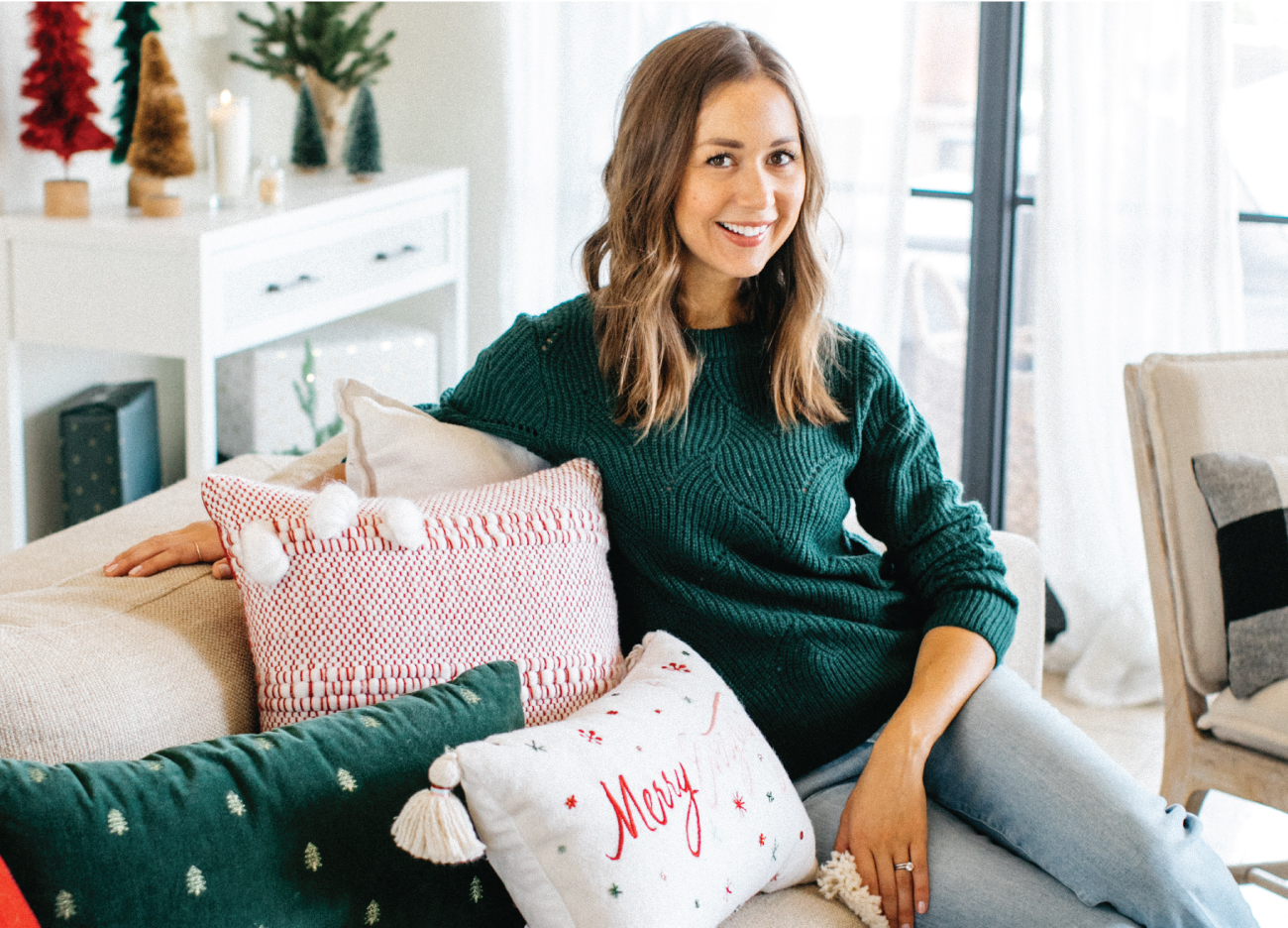 Camille Styles smiles while sitting in a festive living room setting