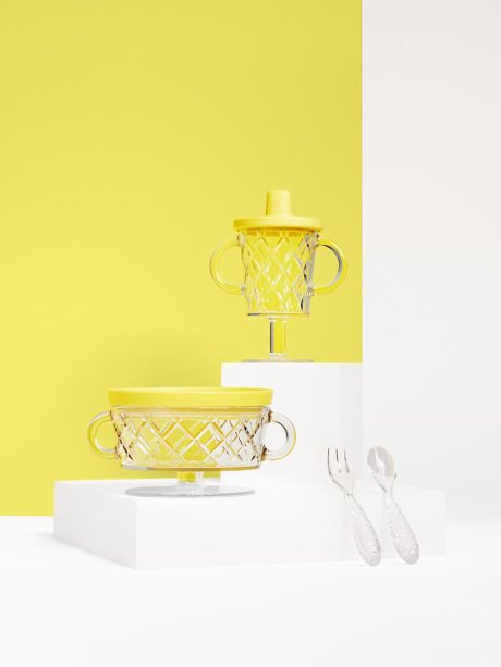 a yellow wall with a lamp and a white table with a gold tray